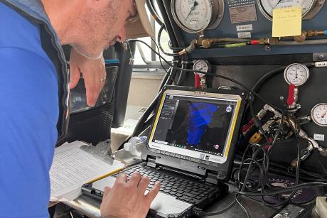 Matt Ogburn in a blue shirt and baseball cap looking at data on a laptop on a boat